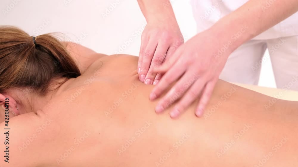 Young woman having massage in spa salon. Close-up of woman relaxing during back massage lying on massage table in slow motion on light background Young woman having massage in spa salon. Close-up of woman relaxing during back massage lying on massage table in slow motion on light background
