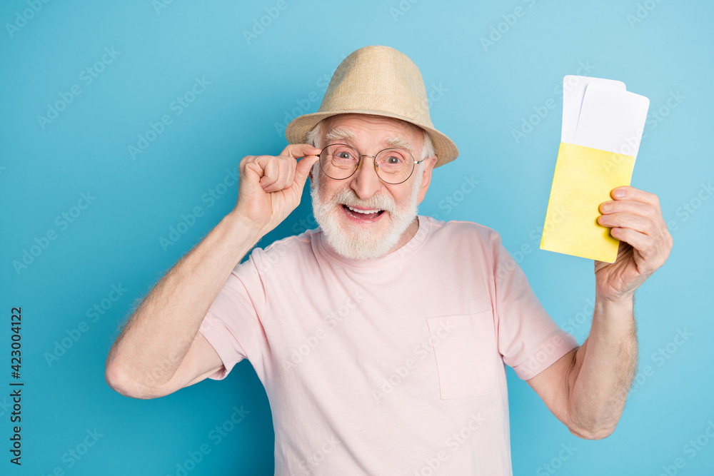 Photo of elderly man happy positive smile hold tickets passport vacation isolated over blue color background Photo of elderly man happy positive smile hold tickets passport vacation isolated over blue color background