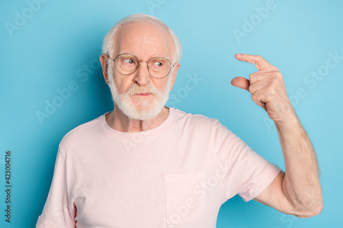 Photo of aged man unhappy upset look show fingers small little size measure isolated over blue color background