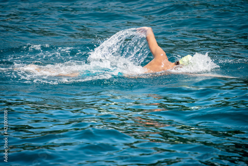 Male freestyle swimmer (front crawl) in the blue waves of the Mediterranean sea, side view. © Alberto Masnovo