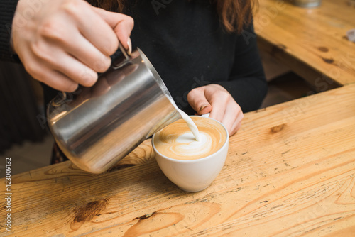 Woman barista makes coffee, pours milk into cappuccino coffee