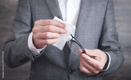 Businessman cleaning eyeglasses with wet wipe.