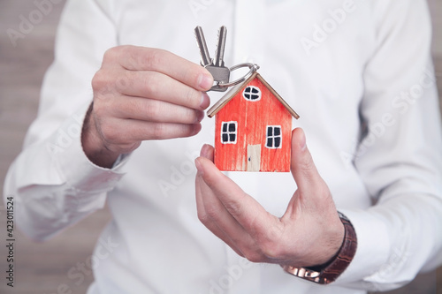 Real estate agent holding wooden house model and keys.