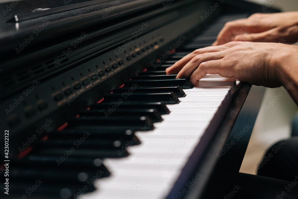 Obraz premium Side view of unrecognizable musician man playing on synthesize at home studio during lesson. Close-up hands of pianist male playing on digital piano in living room. Concept of music education.