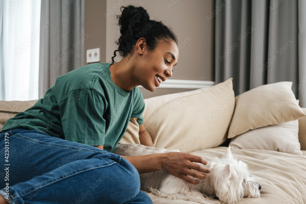 Happy black woman stroking her dog while resting on sofa at home Happy black woman stroking her dog while resting on sofa at home