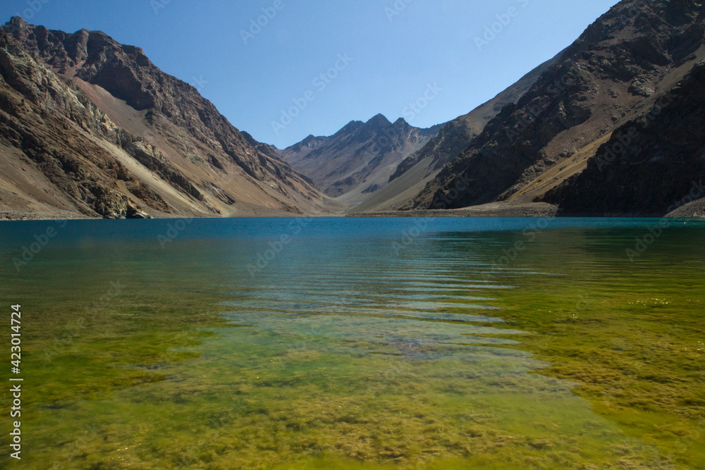 The deep blue color water lake and yellow shallows very high in the Andes mountains. View of the Inca Lagoon in Chile, surrounded by rocky mountains in a summer sunny day.