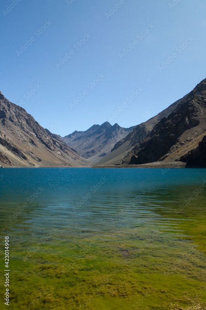 The deep blue color water lake and yellow shallows very high in the Andes mountains. View of the Inca Lagoon in Chile, surrounded by rocky mountains in a summer sunny day.