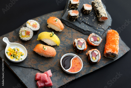 Sushi rolls nigiri, uramaki, hosomaki with salmon  and mango  with soy sauce in a black  stone background