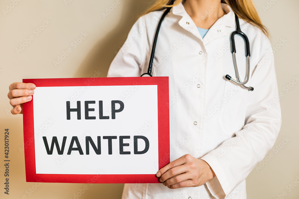 Image of female doctor holding a paper with a text help wanted. Image of female doctor holding a paper with a text help wanted.