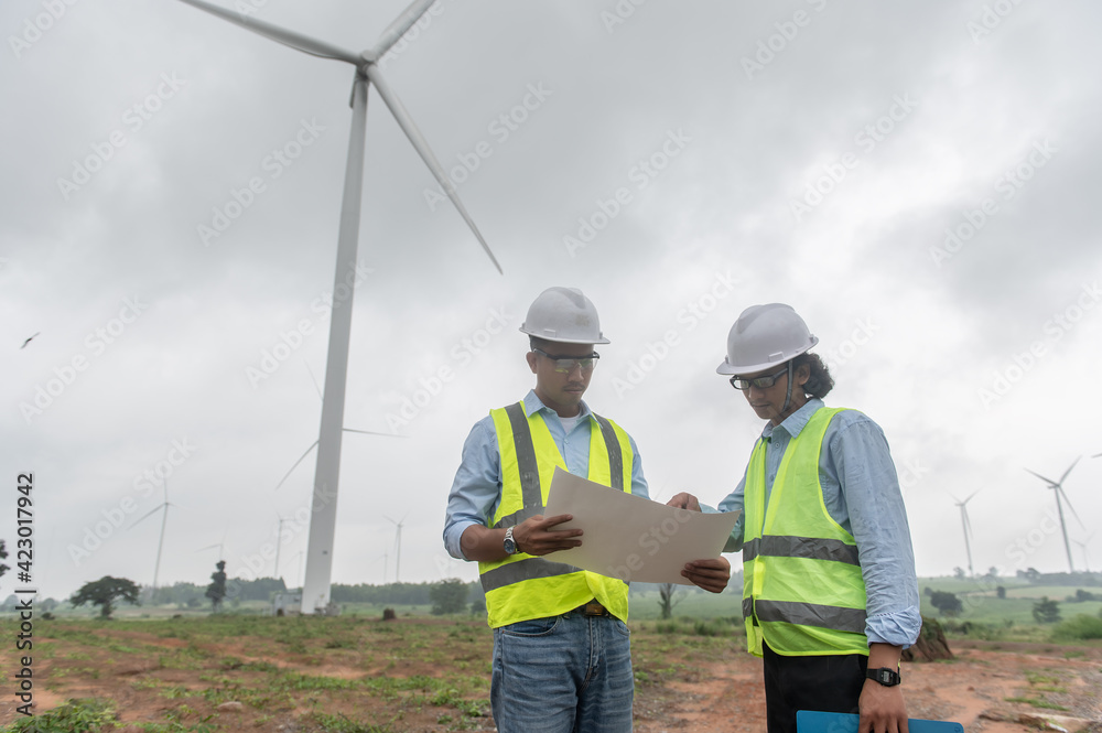 Two engineers working and holding the report at wind turbine farm Power Generator Station on mountain,Thailand people Two engineers working and holding the report at wind turbine farm Power Generator Station on mountain,Thailand people
