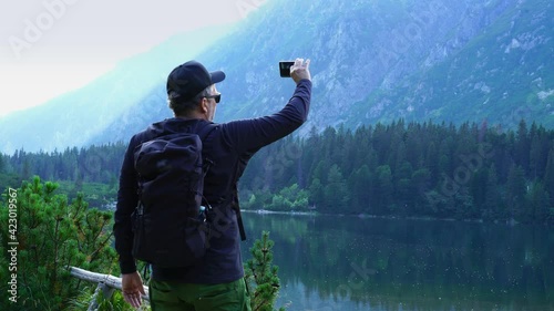 Wallpaper Mural Male tourist uses a smartphone to video a beautiful view in the mountains, Popradske mountain lake, Slovakia, High Tatras Torontodigital.ca
