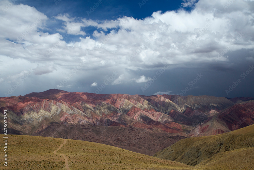 The famous Hornocal colorful mountains in Humahuaca, Jujuy, Argentina. The hiking path across the golden meadow and hills, into the mountain range. Beautiful stone colors and texture.