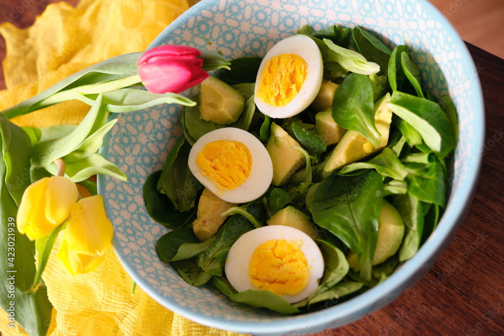 mache avocado salad, egg. In a large bowl on a mahogany wooden table. Yellow scarf and tulip