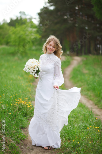 beautiful girl, a blonde in a vintage white dress walks in a blooming apple orchard, a bouquet of anemones, a bride