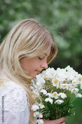 beautiful girl, a blonde in a vintage white dress walks in a blooming apple orchard, a bouquet of anemones, a bride