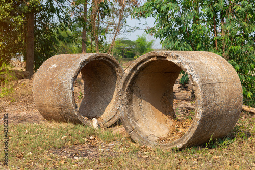 Old concrete pipes. Cracked and deteriorated sewer pipes are left or placed on the ground. On a green tree background.