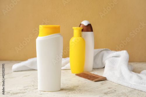 Bottles of different hair cosmetics, towel and comb on color background