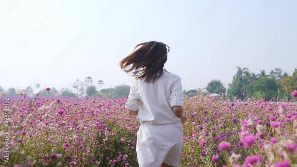 4K Happy Asian woman running in beautiful pink or purple flowers garden farm in springtime. Pretty girl relax and enjoy walking in nature with fresh pink blossom flowers field. People and environment.