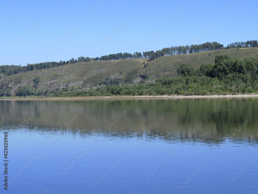 Quiet surface of the river. Beautiful cloudless warm summer day. Mountainous island in the background. Reflection in water