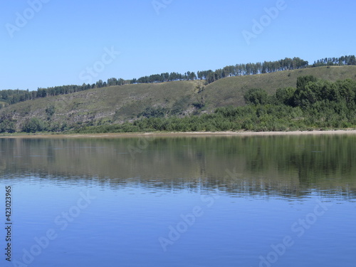 Quiet surface of the river. Beautiful cloudless warm summer day. Mountainous island in the background. Reflection in water