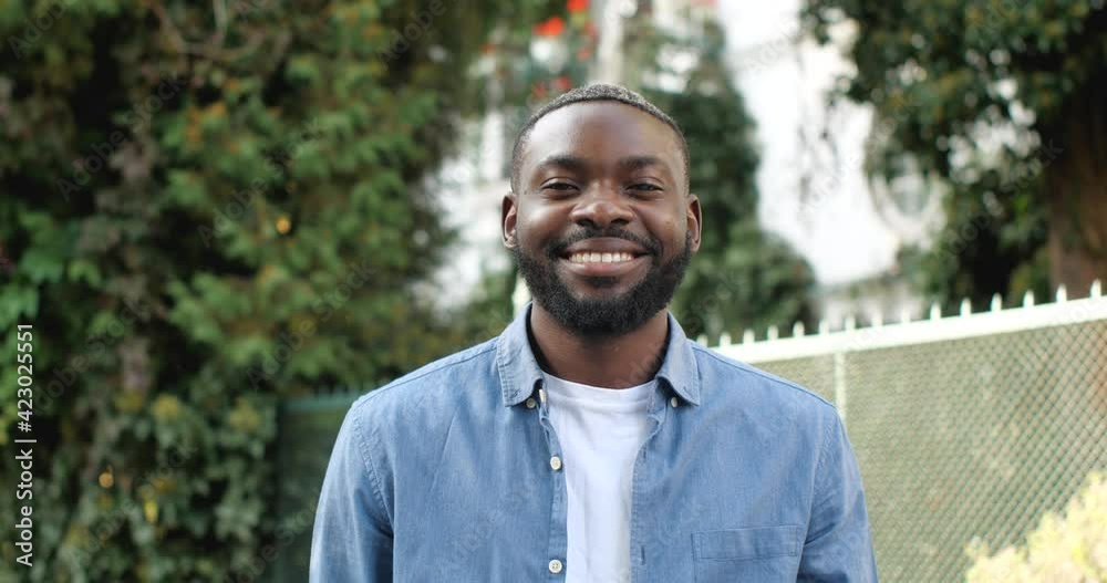 Portrait of Handsome African Guy with Healthy Smile Looks at the Camera. Having Good Mood Posing at the Park. Wearing Casual Clothes having Attractive Appearance. Confident Male. Vacation. Portrait of Handsome African Guy with Healthy Smile Looks at the Camera. Having Good Mood Posing at the Park. Wearing Casual Clothes having Attractive Appearance. Confident Male. Vacation.