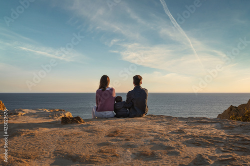 Family sitting on the cliff and enjoy sunset or sunrise. Three People Man Woman and Child sitting on the cliff and Ocean Horizon on Background.