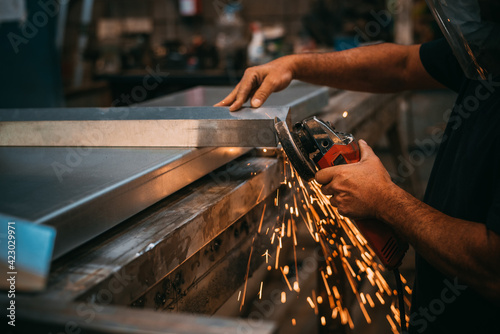 Fotografie an adult man is seen working cutting a piece of metal in an industrial workshop,