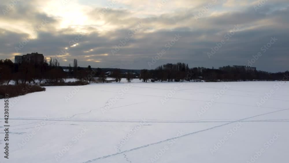 Aerial flying up on frozen wintery river covered in snow with scenic epic cloudy sky in winter. Fast moving clouds in sunset cold sky Aerial flying up on frozen wintery river covered in snow with scenic epic cloudy sky in winter. Fast moving clouds in sunset cold sky