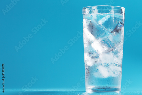 A glass with ice and clean water on a blue background.