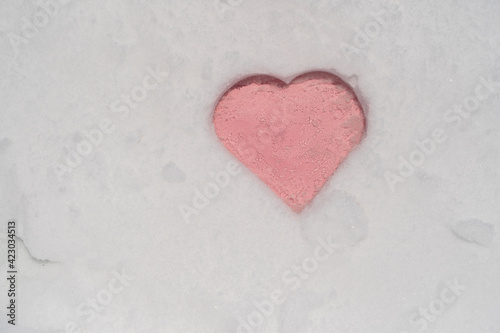 Pink heart shape on a white fresh snow in winter, close up