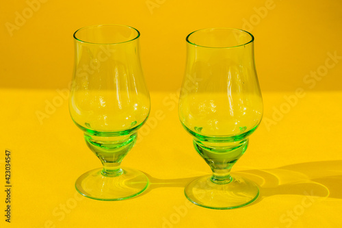 two empty green goblets of glass stand on a yellow background. Horizontal photo, close-up.