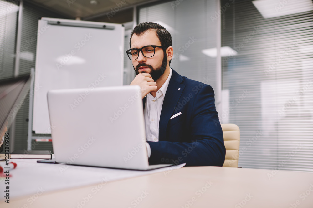 Serious businessman working on laptop in contemporary workspace Serious businessman working on laptop in contemporary workspace