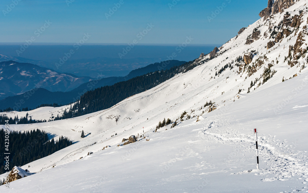 Snowy hiking trail in Bucegi mountain range down to the valley - Romania