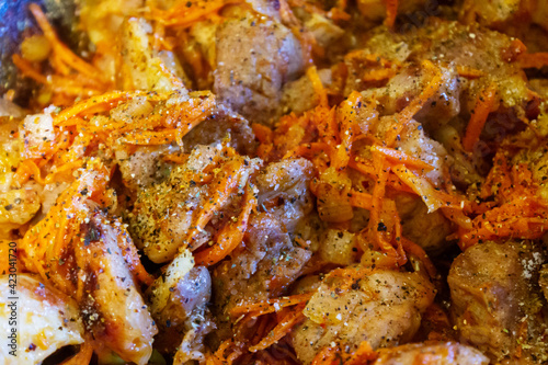 Roasted meat with carrots and onions close-up and spices.