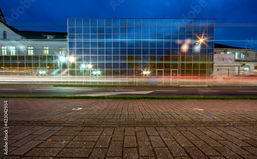 Longa exposição noturna com faróis dos carros riscando a imagem, com edifício geométrico espelhado à frente. photo