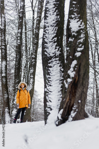 caucasian woman in orange jacket walking in a winter park in the middle of the trees in nature, enjoying the walk and the winter scenery and silence © MyJuly