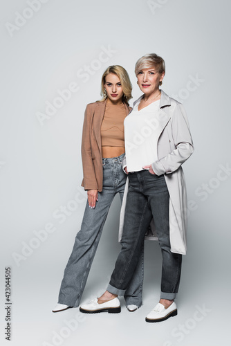 fashionable mother and daughter looking at camera while posing on grey