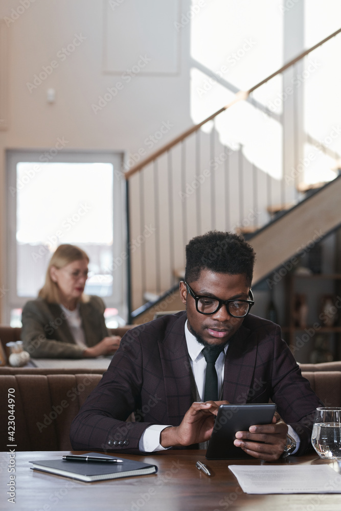 African young businessman using digital tablet while working online sitting in coffee shop