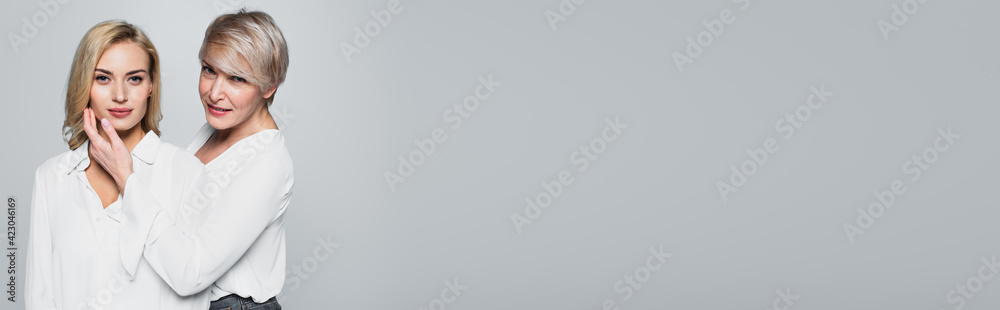 middle aged woman in white blouse touching face of young daughter isolated on grey, banner middle aged woman in white blouse touching face of young daughter isolated on grey, banner