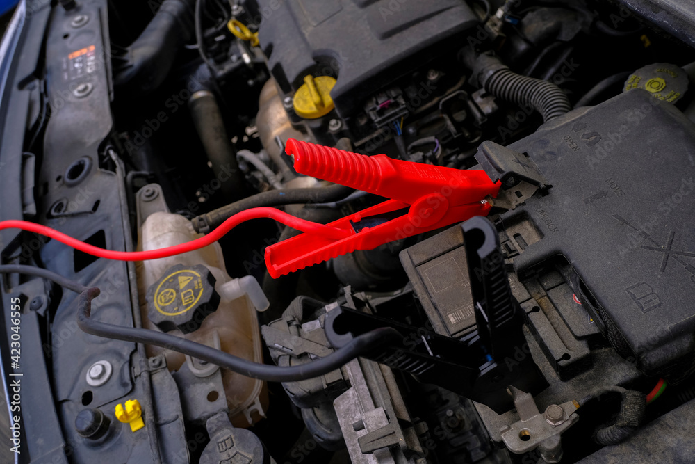 car service inside car close-up. Car battery charger device across open hood. Car bonnet top view