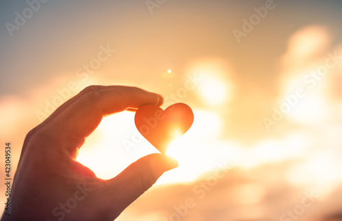 Hand holding heart on a warm colorful sky background