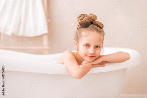 Baby girl sitting in the bathroom. Portrait of a cute girl in sunglasses in a bright bathroom.