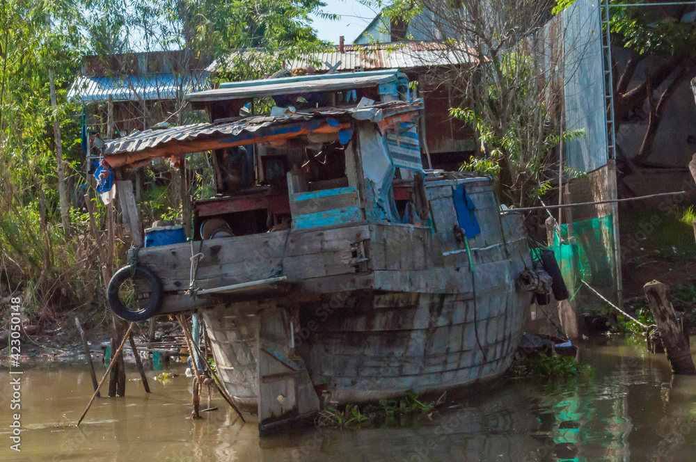 altes, zerfallendes Fischerboot liegt am Ufer des Mekong. Im Hintergrund, Häuser aus Wellblech