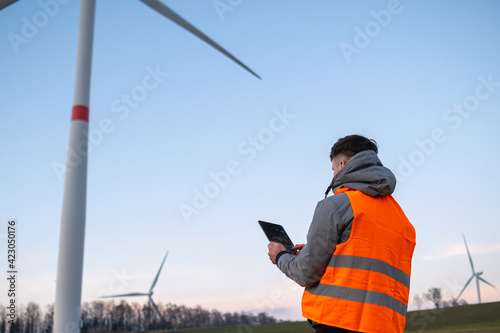 Windmill engineer does maintenance and repairs wind turbines using a tablet in the orange vesta.