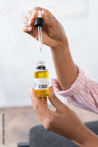 cropped view of african american woman holding bottle with cbd lettering and pipette