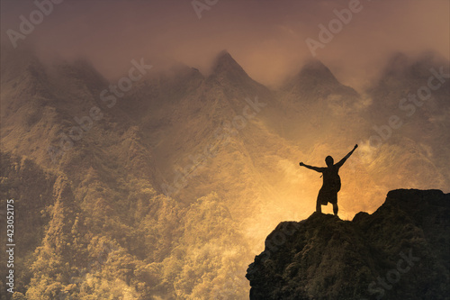 silhouette of a person on a mountain with arms up to the sky 