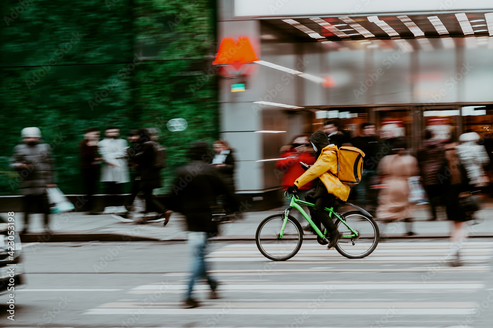 Obraz premium Blurred image of a food delivery courier delivering food on bicycle. Cyclist carrying backpack with food and drinks. Fast delivery within the city with the shortest possible time