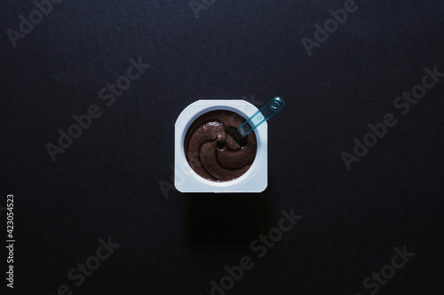 Top view of chocolate pudding with a plastic spoon isolated on a black background
