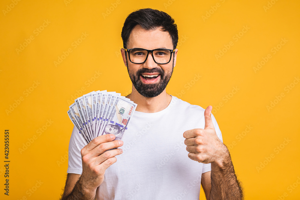 Happy winner! Young rich man in casual holding money dollar bills with surprise isolated over yellow background. Happy winner! Young rich man in casual holding money dollar bills with surprise isolated over yellow background.