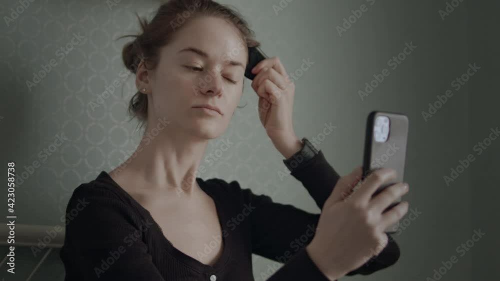 Close-up of young beautiful woman doing facial massage using Gua Sha stone. She is sitting on her bed, massaging skin and using smartphone. Close-up of young beautiful woman doing facial massage using Gua Sha stone. She is sitting on her bed, massaging skin and using smartphone.